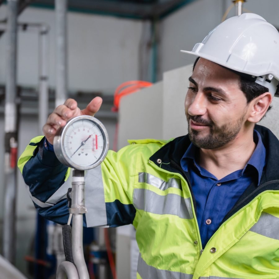 Young male machine inspector wearing vest and hardhat with headphones checking machine and sterilizers in water plant while making notes in digital tablet